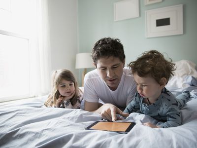Father and children using digital tablet in bed