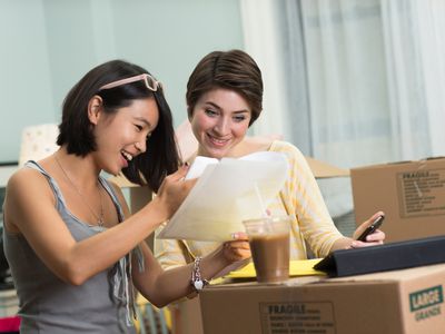 两名年轻女子在搬家箱的包围下寻找新公寓的文件。