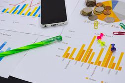 Close-Up Of Bar Graphs With Mobile Phone And Office Stationery