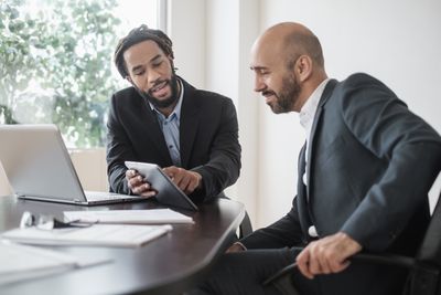 Two businessmen working with digital tablet by desk in office