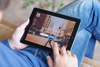 屏幕上的linkedin持有iPad的男人“width=