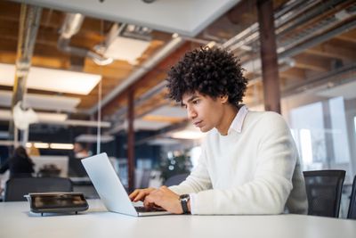 Young adult in white shirt working on laptop in his office