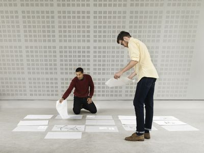 Project managers setting the flow of a project by laying out information pages on the floor of an office.