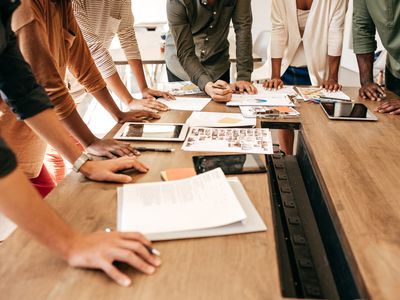 Advertising team standing around a table during a meeting while one worker writes on a chart.