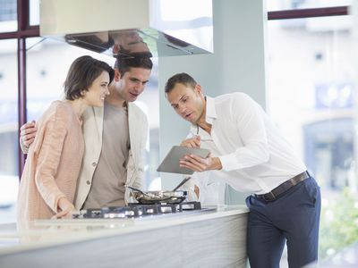 Mid adult couple and salesman looking at digital tablet in kitchen showroom