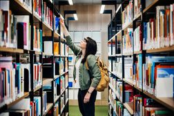 Student Selecting Book From Shelf In Library