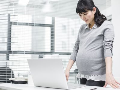 一位孕妇站在办公桌前阅读客户的孕妇电子邮件，然后再发送。