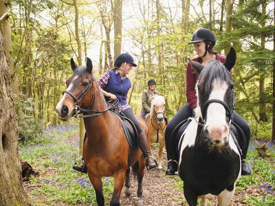 Therapeutic riding instructor with a student on horseback on a forest path.