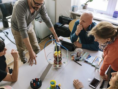 A project manager explains a client's cost overrun problem with their team at a table.