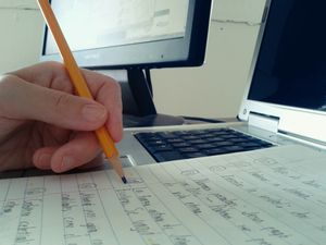 person writing on paper in front of computer