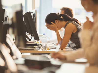 Stressed businesswoman with head in hands at office desk, considering a voluntary demotion.