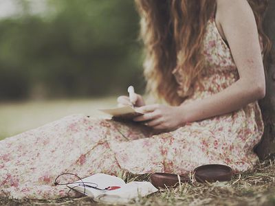 A woman sitting against a tree writing a letter
