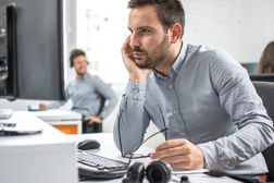 Man looking at computer screen and keeping his eyeglasses while sitting at his working place in office.