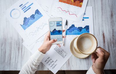 person using phone and graphs to analyze finances