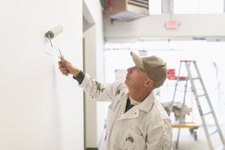 A skilled painter in overalls painting a wall using a roller brush.