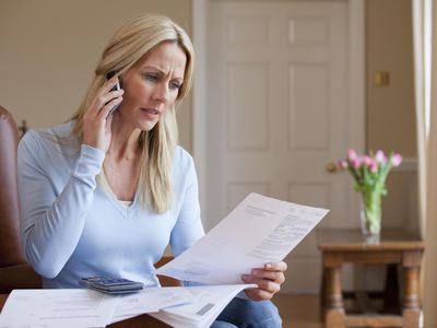 Concerned woman holding bills and talking on cell phone