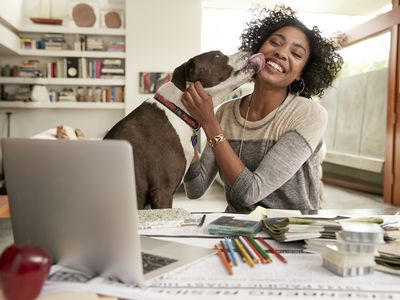 dog licking woman's face sitting in front of a computer