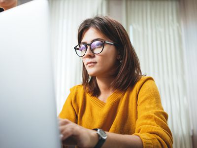 沉思的女商人在办公室工作场所戴眼镜。年轻英俊的女工使用现代笔记本电脑