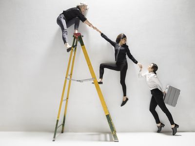 A step ladder with a person on top helping a person mid-way up climb the ladder who is helping someone on the ground.