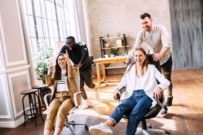 Teammates push each other in office chairs during a team building exercise.