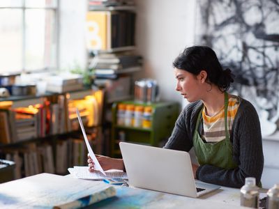 Young artist in her studio filling out grant application on laptop