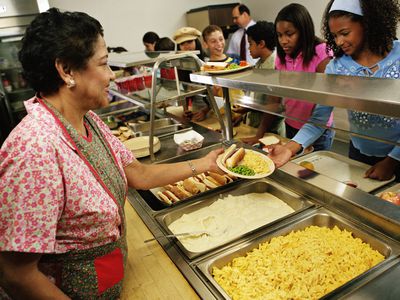 Mature woman serving food to students (12-14) in cafeteria