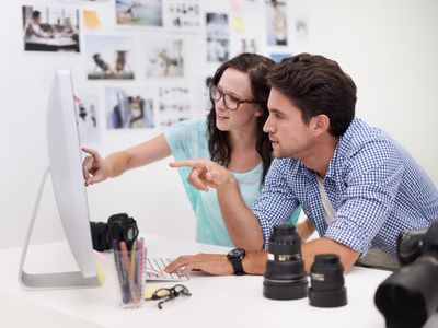 Two model bookers pointing at photos on a computer monitor.