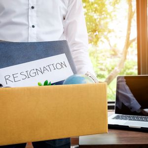 Person carrying a box of belongings with a letter of resignation on the top.