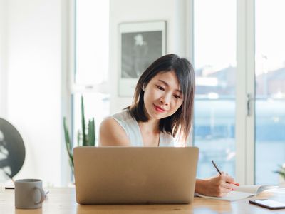 Young woman taking notes while having a video conference using laptop at home