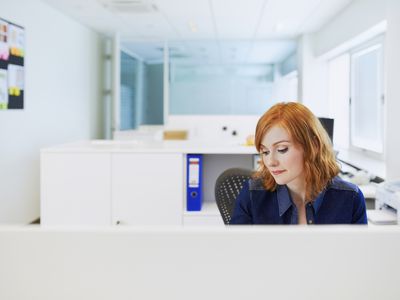 A young woman sitting in her office cubicle with other cubicles in the background.
