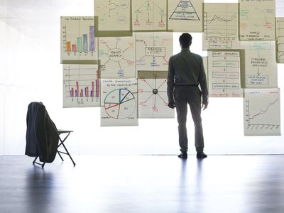 Project manager looking at charts pinned to a wall.