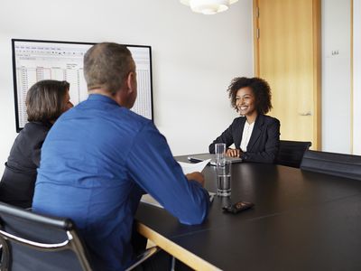 A woman sitting across the table from two people as she interviews for a job in sales.