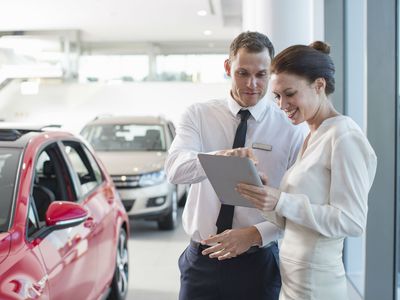 Salesman and female customer using digital tablet in car dealership