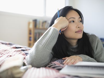 Pensive woman with pencil journaling, looking away on bed
