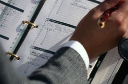 Close up of man writing in a day planner representing time management.
